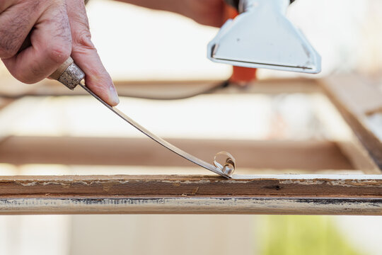 Carpenter using heat gun and wood scraper removes paint from old wooden window. Construction industry, carpentry. Restoration. 
