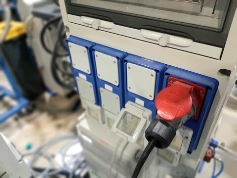 Industrial three phase power plugs and sockets on factory wall. Electrical cables connected to heavy duty red high voltage outlets in workshop background.