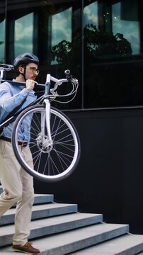 Man carries bicycle downstairs near dark glass office building