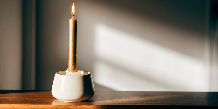 gold taper candle in cream ceramic holder on a dark walnut mantel