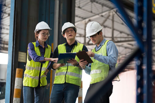 Workers, warehouse storage and logistics. Diverse group of warehouse workers wearing safety hard hats discussing inventory management and operations logistics planning in industrial storage warehouse