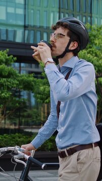 Man drinks coffee while walking bicycle through office plaza