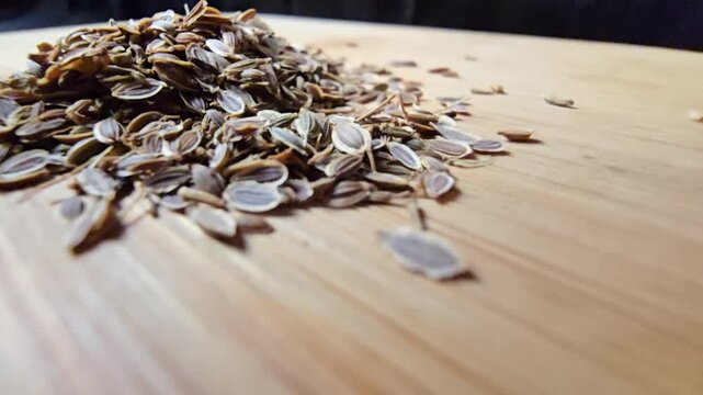 A low-angle macro shot moving smoothly towards a pile of dried dill seeds scattered on a wooden cutting board
