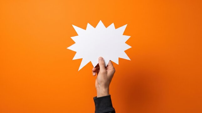 Hand holding a blank white speech bubble sign over an orange background