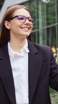 Young woman greeting a colleague with a friendly wave while walking through a city park and talking on her smartphone. Slow motion