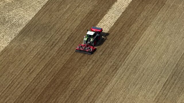 Modern tractor pulling a seed drill through dry soil on vast agricultural farmland, preparing fertile ground for planting crops during seasonal farm work on sunny day