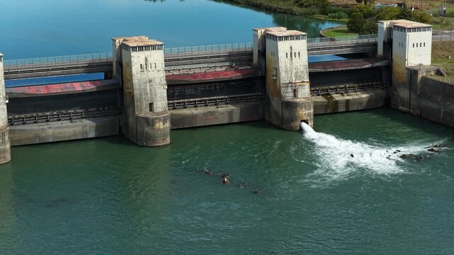 Massive concrete dam releasing a powerful stream of turbulent white water through a drainage sluice gate into the green river reservoir on a bright sunny day