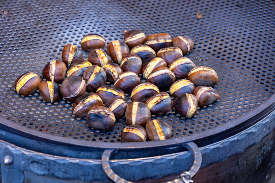 Roasted chestnuts on a perforated metal grill at a street stall in Rome, Italy, autumn food close-up