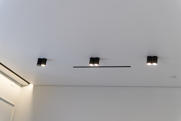 Modern black ceiling spotlights and linear slot on white stretch ceiling in minimalist interior © Sergey