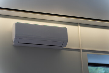 White wall mounted split air conditioner under ceiling cornice with warm lighting indoors © Sergey
