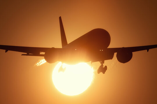 View of a commercial airplane silhouetted against the large glowing sun during sunset at Amsterdam Airport Schiphol, Schiphol, North Holland, Netherlands.