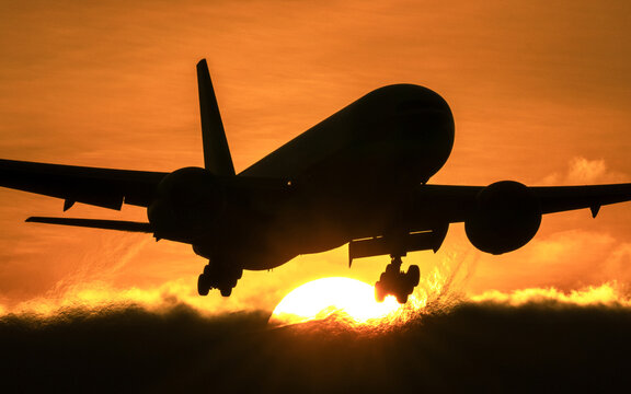 View of a passenger airplane silhouette landing against a vibrant sunset sky at Amsterdam Airport Schiphol, Schiphol, North Holland, Netherlands.