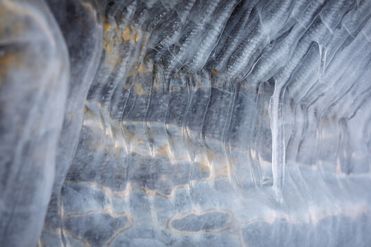 View of Lake Baikal featuring intricate ice formations and translucent icicles hanging from a frozen cave wall in Russia.