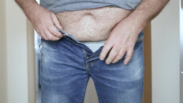 Overweight Man Struggling to Fasten Belt on Jeans Closeup. Man with Big Belly Trying to Buckle Leather Belt.