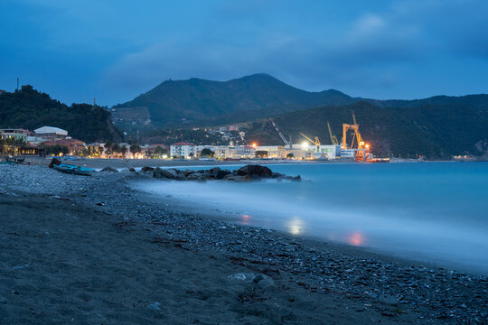 View of Fincantieri S.p.A. shipyard at twilight with a pebble beach in the foreground and calm sea in Sestri Levante, Liguria, Italy.