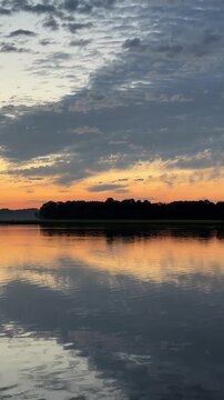 Blue clouds and an orange sunset band mirrored on a calm river, vertical HD