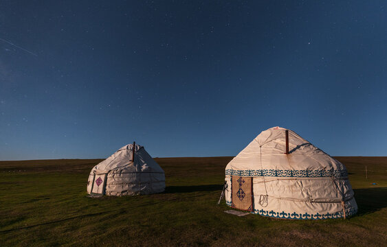 View of two traditional yurts set in a grassy field under a clear starry night sky at Song-Kul, Naryn Region, Kyrgyzstan.