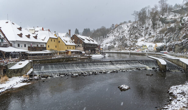 View of the Vltava River flowing past historic buildings covered in snow in Cesky Krumlov, South Bohemian Region, Czechia.