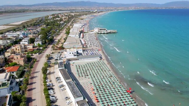Aerial drone forward shot along Poetto beach in Cagliari, Sardinia, Italy, with turquoise sea, colorful beach umbrellas and seaside promenade in summer