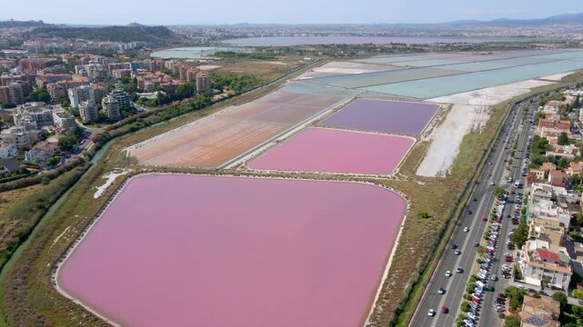 Aerial drone rising shot over pink salt pans of Cagliari, Sardinia, Italy, with Molentargius salt ponds, coastal road and city in the background