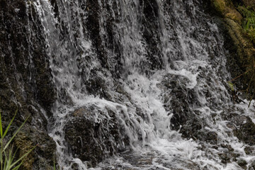 Waterfall cascading down dark mossy rocks with splashing white foam and fresh flowing water close up © Oleg