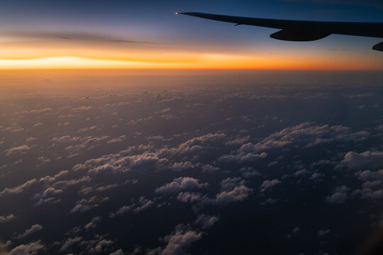 View of an airplane wing silhouetted against a vibrant sunset sky above a vast layer of clouds over Mexico.