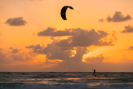 View of a kitesurfer riding a hydrofoil board on the ocean during a vibrant golden hour sunset with clouds in the sky, Mexico.