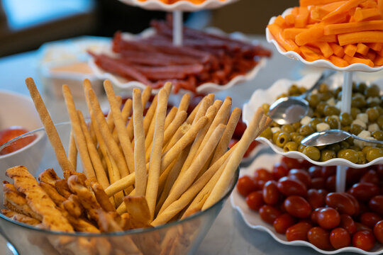 View of a catering spread featuring a glass bowl filled with breadsticks, alongside tiered platters of cherry tomatoes, green olives, and carrot sticks in London, United Kingdom.