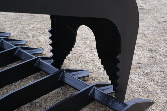 Serrated black steel grapple jaw and tines close up on dry grass