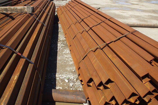 Strapped bundles of rusty square steel tubing in a yard
