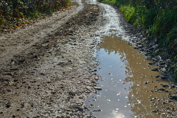 Muddy puddle on a dirt country road with wet tire tracks and stones, showing a rural path after rain in autumn. © beautiful-photo.de