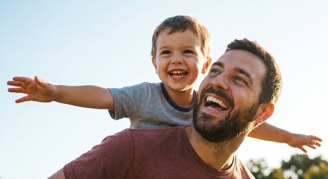 Cheerful father giving son a piggyback ride outdoors while playing airplane together in sunny weather, enjoying family bonding, laughter, and quality time