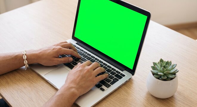 Close up of hands typing on laptop computer featuring blank chroma key green screen for modern digital workspace