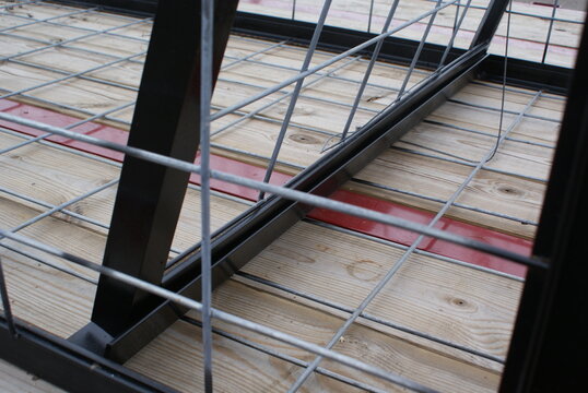 Inside a black steel welded wire cage on a wooden trailer deck