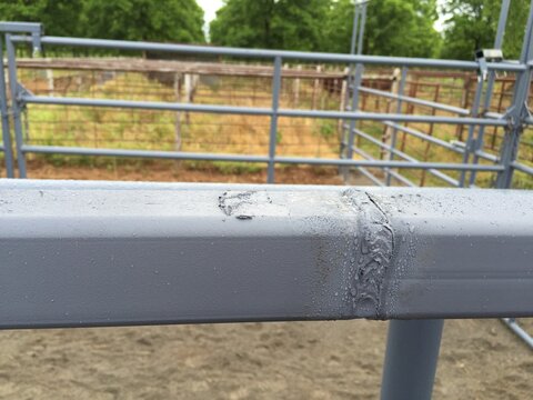 Rain droplets on a welded seam of a gray steel corral rail