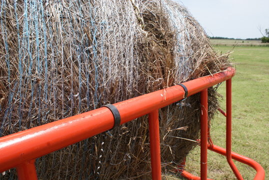 Orange steel hay ring wrapped around a round bale in a green field