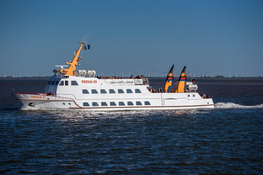 Modern passenger ferry navigating coastal waters under a clear blue sky. The vessel creates a visible wake while traveling across the sea, showcasing maritime transportation, tourism, and regional fer