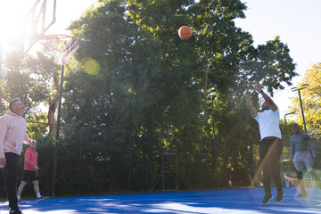 Group of men playing basketball on blue court, white T-shirt player shooting at hoop, copy space © WavebreakMediaMicro
