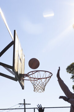 Players reaching and jumping near outdoor basketball hoop at local court, ball flying above rim