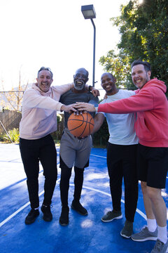 Diverse male friends posing on blue basketball court, holding basketball and wearing athletic gear