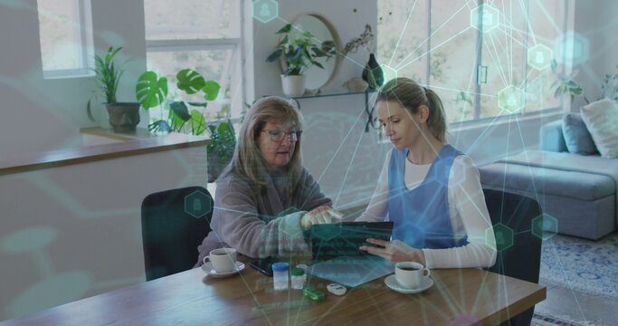 Pointing caregiver wearing blue vest and senior woman holding tablet at home, with glucose meter