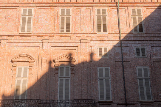 View of the historic brick facade of the Royal Palace with symmetrical windows, shutters, and an iron balcony in Turin, Piedmont, Italy.
