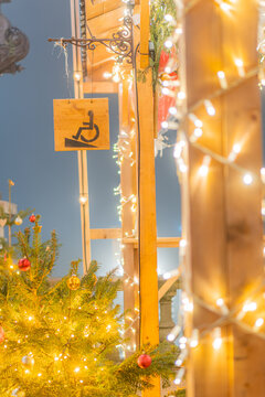 View of a wooden Christmas market stall decorated with glowing fairy lights and ornaments, featuring a hanging wheelchair access sign