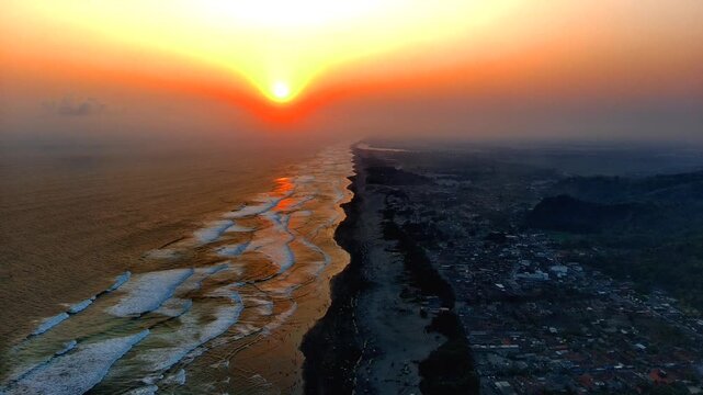 Aerial view of Parangtritis Beach at sunset with golden light reflecting on the waves along the coastline in Kecamatan Kretek, Daerah Istimewa Yogya, Indonesia.
