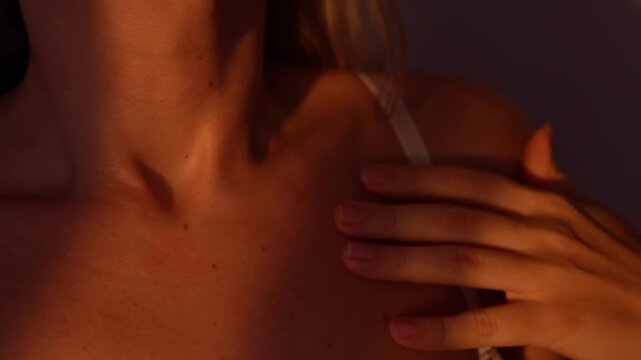 Young woman gently sliding her fingers along her chin, neck, collarbone and shoulder. Sensual closeup of delicate skin and graceful feminine movements in soft warm light