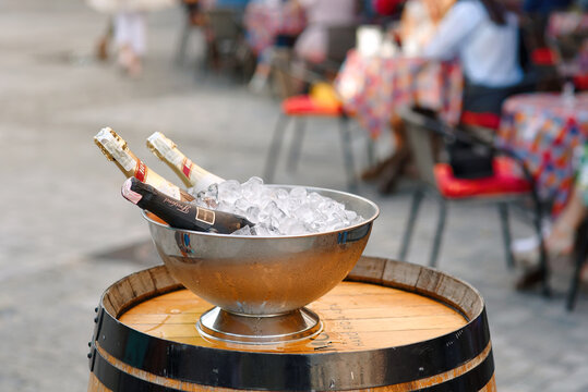 Minsk, Belarus. Aug 5, 2018. Cold sparkling wine bottles resting in an ice bucket on vintage wooden barrel outside summer cafe terrace. Festive setup of champagne bottles chilling in an ice bucket