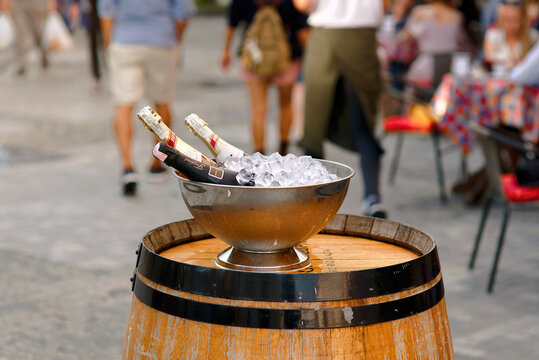 Minsk, Belarus. Aug 5, 2018. Three chilled bottles of champagne resting in metal ice bucket on wooden barrel table outside bustling summer street cafe. Sparkling wine bottles cooling in an ice bucket
