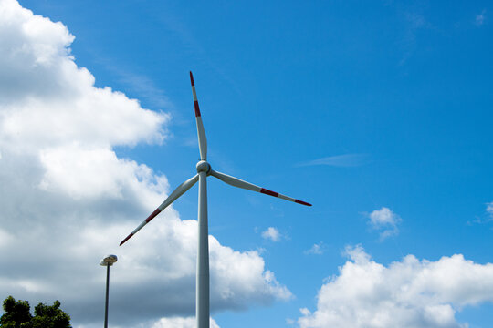 View of a wind turbine standing against a bright blue sky with fluffy white clouds in Breitenbach, Rhineland-Palatinate, Germany.