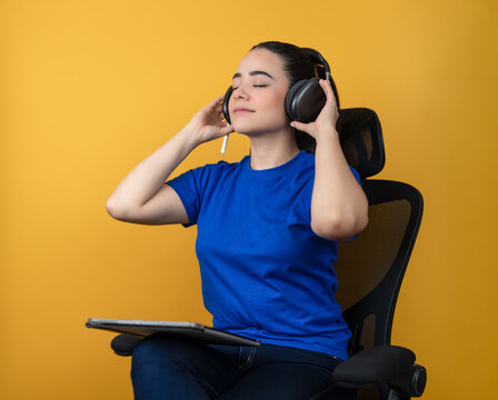 Woman wearing headphones, relaxing with eyes closed and enjoying music in an office chair