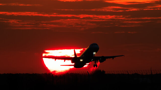 View of a passenger airplane silhouette taking off against a vibrant red sunset at Bucharest Henri Coanda International Airport in Otopeni, Judetul Ilfov, Romania.